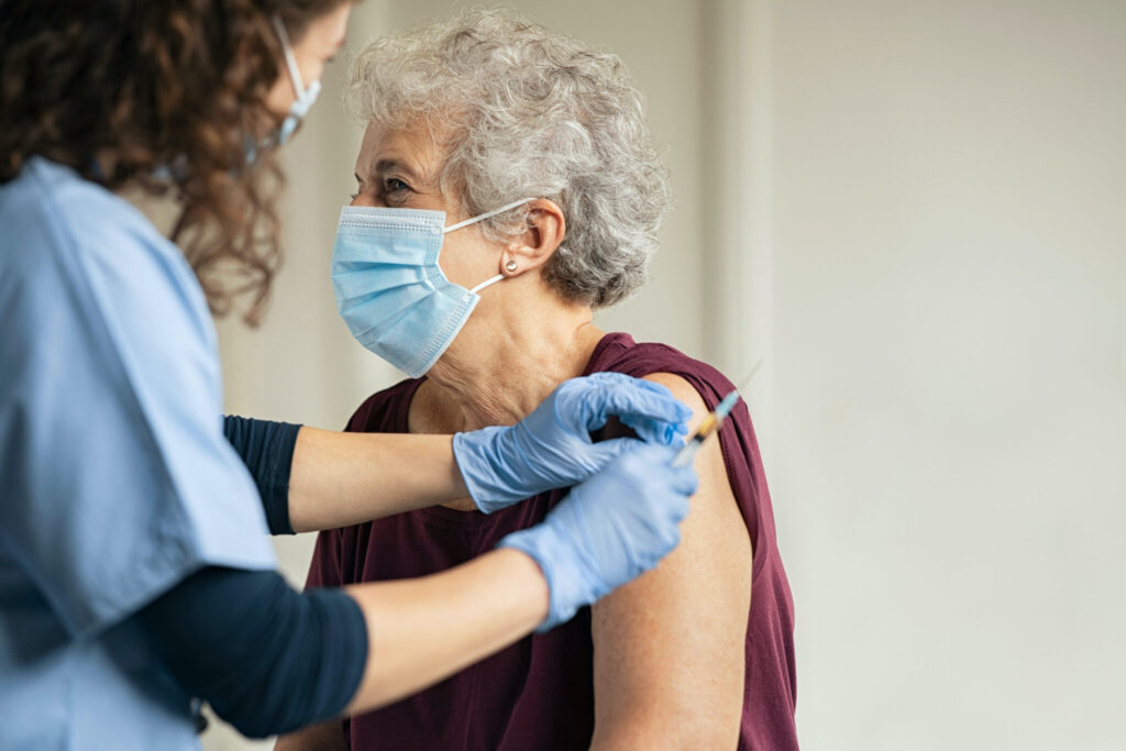 General practitioner vaccinating old patient in private clinic with copy space. Doctor giving injection to senior woman at hospital. Nurse holding syringe and using cotton before make Covid-19 or coronavirus vaccine.